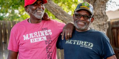 Two smiling elderly men wearing military-themed shirts and hats.