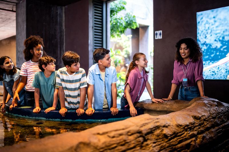 Child students talking and interacting with marine life in touch pool at aquarium