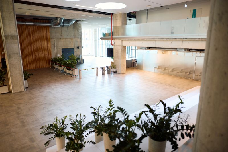 Wide view of an empty modern office lobby with turnstiles, potted plants, and a mezzanine floor, showcasing a minimalist and contemporary design