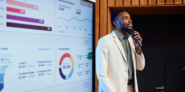Man presenting business data on a large screen during a meeting.