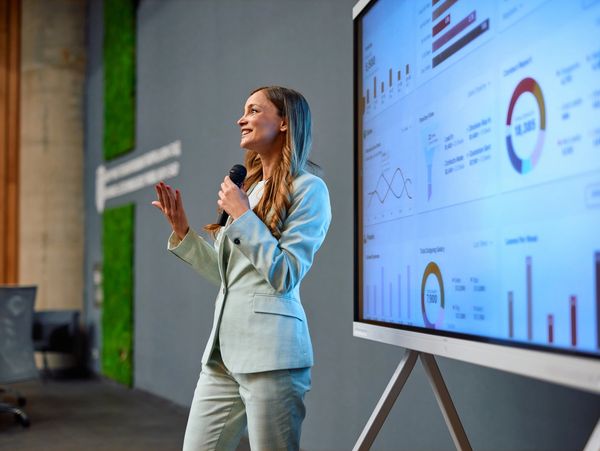 Businesswoman giving a presentation with data charts on a large screen.