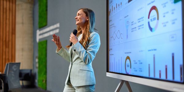 Businesswoman giving a presentation with charts on a large screen.