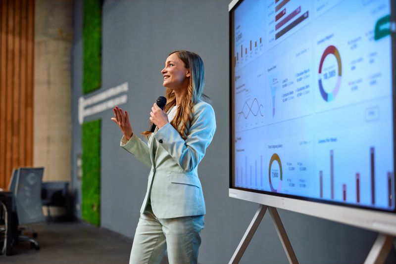 Young businesswoman using a microphone and presenting marketing data using an interactive whiteboard during a business conference in a modern office