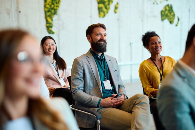 Group of diverse business professionals attentively listening during a corporate training session in a modern office, promoting teamwork and career development
