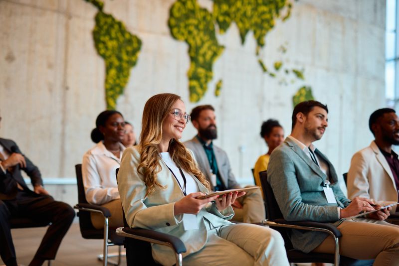 Group of businesspeople attending a seminar and listening to a presentation about global business and sustainability, with a world map made of plants in the background