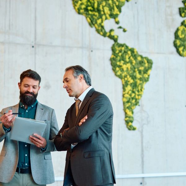 Dos hombres de negocios conversando frente a un mapa verde del mundo.