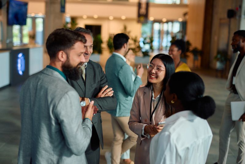 Group of multi-ethnic business professionals networking and engaging in conversations during a corporate event held in a spacious lobby, fostering connections and collaboration
