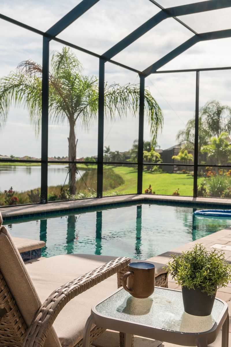 Lounge chair beside blue swimming pool in suburban Florida home with screened enclosure and palm trees.