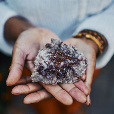 Hands holding a large amethyst crystal cluster.