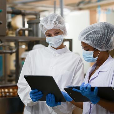 Two masked food factory workers reviewing data on tablets.