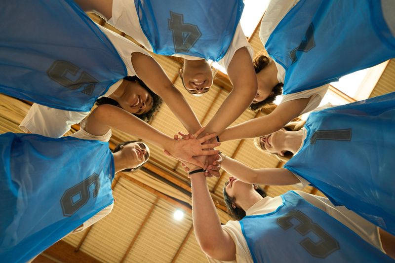 Female basketball players joining hands in a circle before a game, embodying teamwork, unity, and the spirit of competition