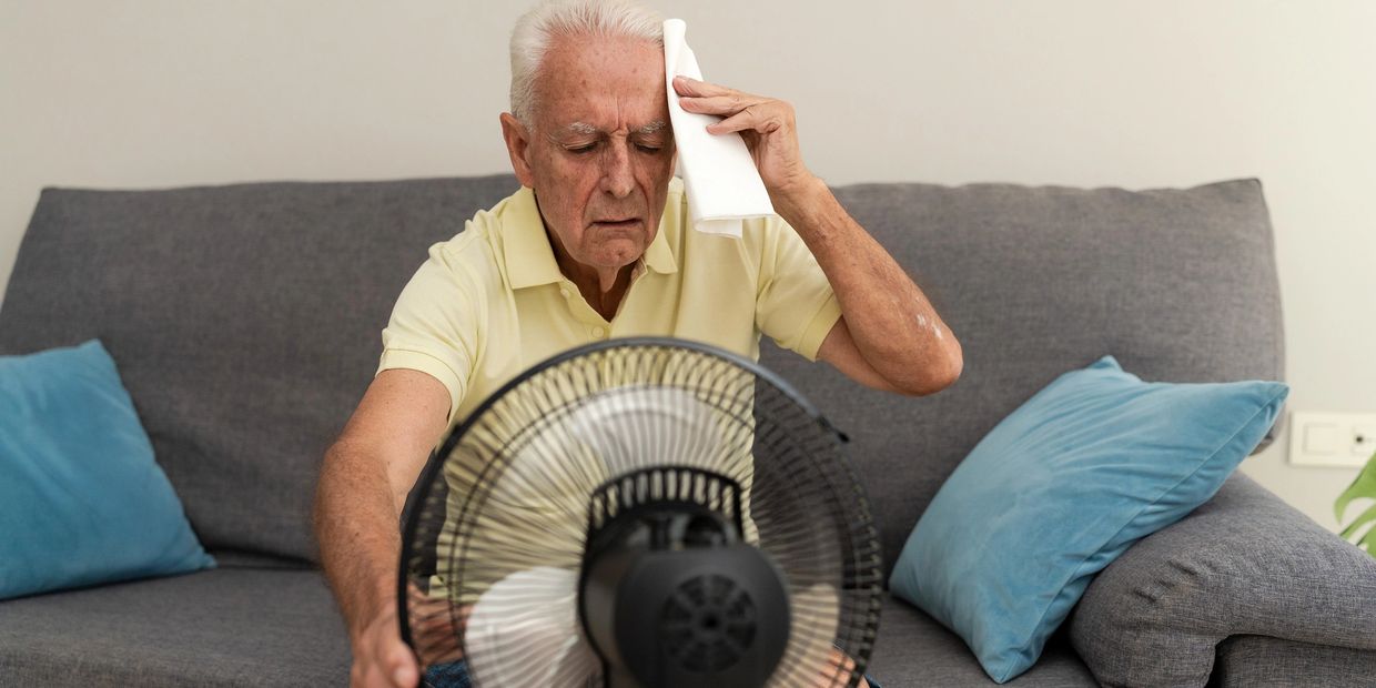 Elderly man cooling off with a fan and wiping sweat.