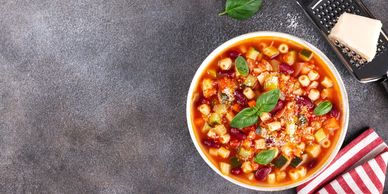 A bowl of vegetable minestrone soup garnished with basil leaves and grated cheese.