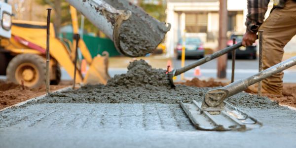 Construction workers pouring and smoothing fresh concrete on a sidewalk.