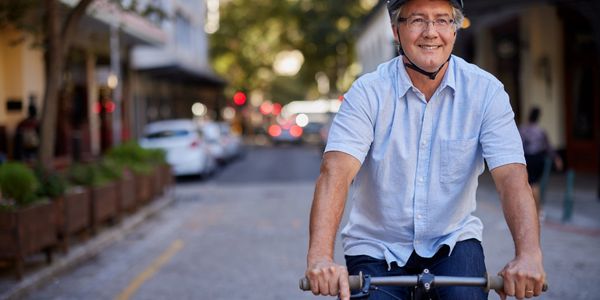 Smiling middle-aged man rides a bicycle wearing a helmet on a city street.