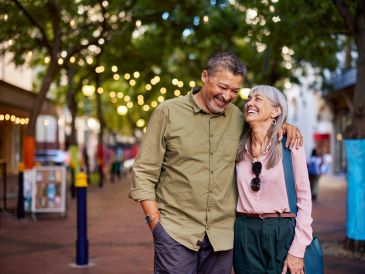 Elderly couple enjoying a walk outdoors, smiling warmly at each other.
