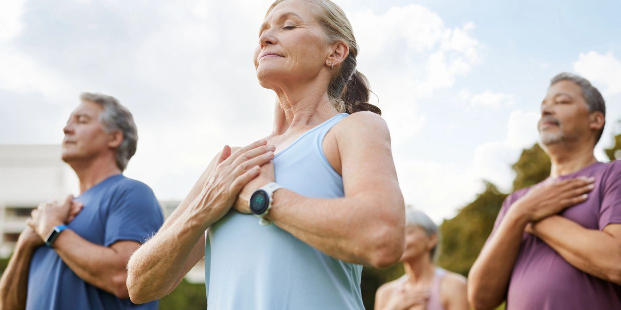 Group of adults meditating outside with hands on chest.