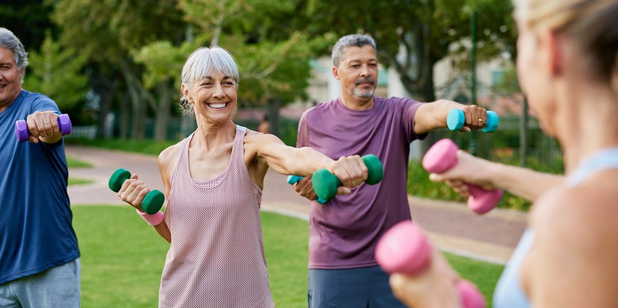 Seniors exercising outdoors with dumbbells, smiling and stretching.