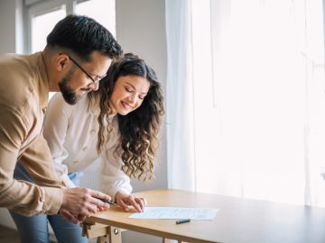 A happy couple reviewing documents together at a table near a window.