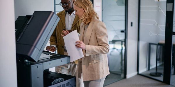 Two colleagues using a printer in an office environment.