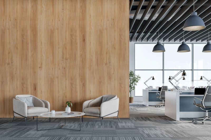 Contemporary office interior featuring a cozy lounge area with armchairs and coffee table, light wood wall panels, and an open-plan workspace with desks, task chairs, and desk lamps. Large windows provide natural daylight, and the minimalist design is ideal for corporate, coworking, or business-related themes. 3D rendered image