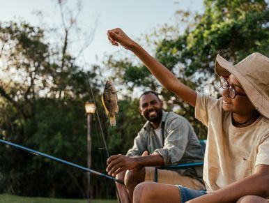 Smiling child holding up a caught fish while fishing with an adult.