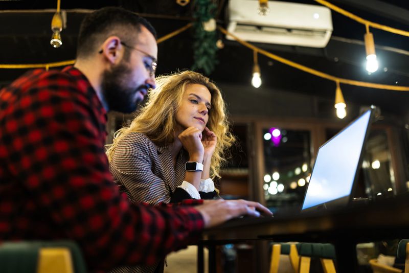 Two colleagues intensely collaborating on a project using a laptop in a cozy cafe. The warm lighting and relaxed atmosphere enhance their focus and teamwork.