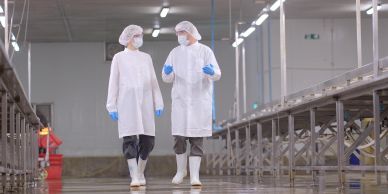 Two workers in protective gear walking and talking in a clean factory environment.