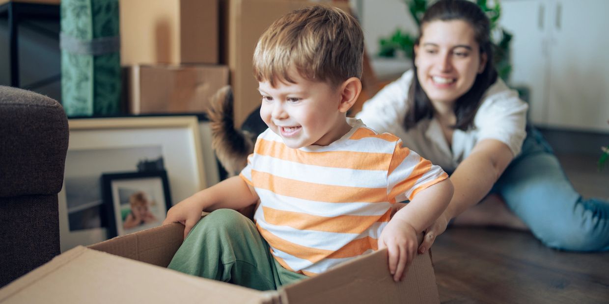 A child enjoys sitting in a cardboard box while a woman happily pushes him.