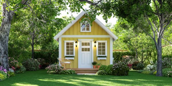 Charming yellow cottage surrounded by lush greenery and trees.