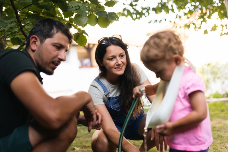 Loving parents spending quality time in the garden with their child. The candid moment shows family bonding, parenting joy, and the simple joys of outdoor play under the warm sunlight.