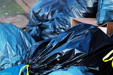 Pile of tied black and blue garbage bags on a sidewalk.