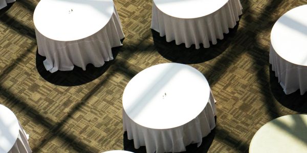 Round tables with white tablecloths casting shadows on patterned floor.