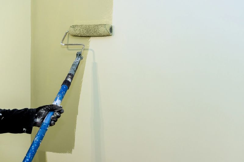 Carpenter paints wall with roller, working on home renovation project in bright living area.