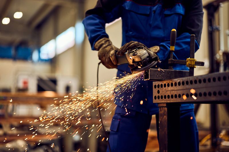 A worker uses a grinder on metal, producing sparks in an industrial workshop.
