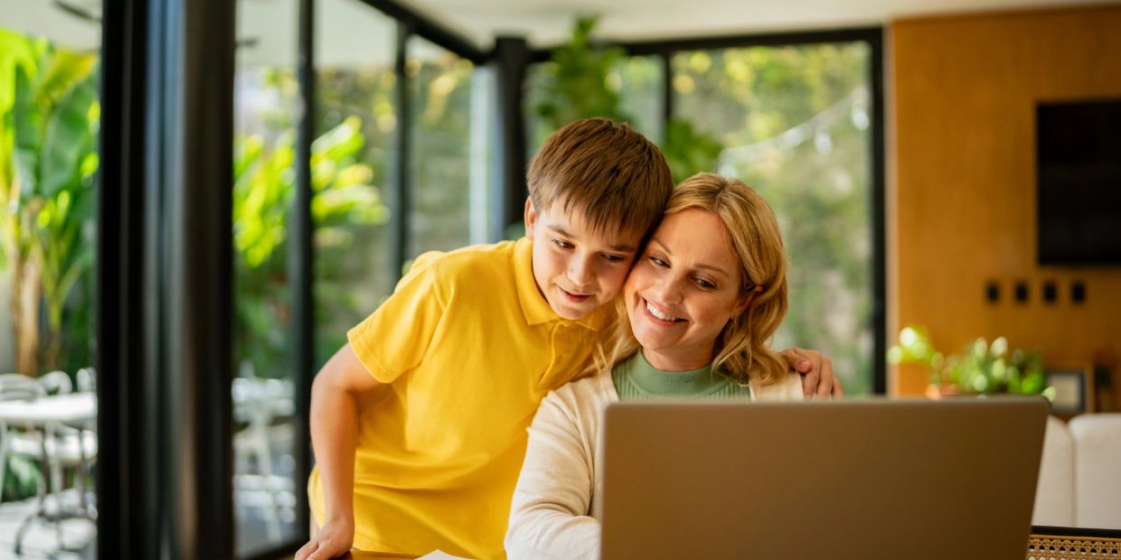 A smiling woman and boy looking at a laptop together indoors.