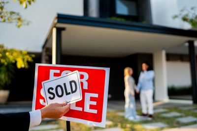 Hand holding a sold sign in front of a for sale sign.