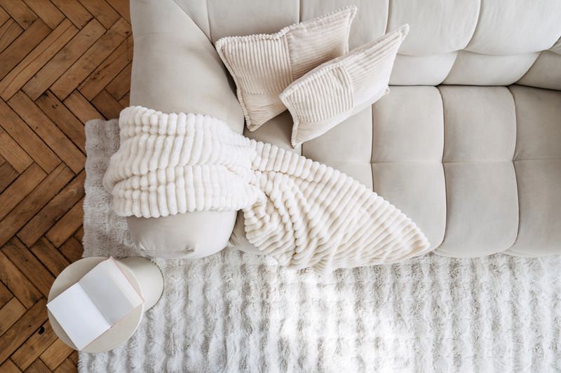 Top view of stylish modern room interior showcases a comfortable white couch adorned with soft pillows and a cozy blanket. Natural light illuminates the living space. Open book on side table
