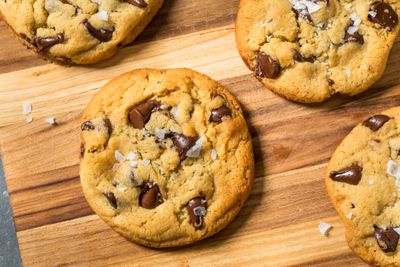 Freshly baked chocolate chip cookies on a wooden board sprinkled with sea salt.