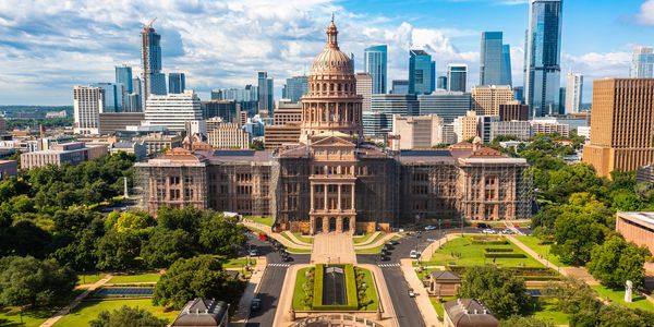 Austin's Texas State Capitol with city skyline background on a sunny day.