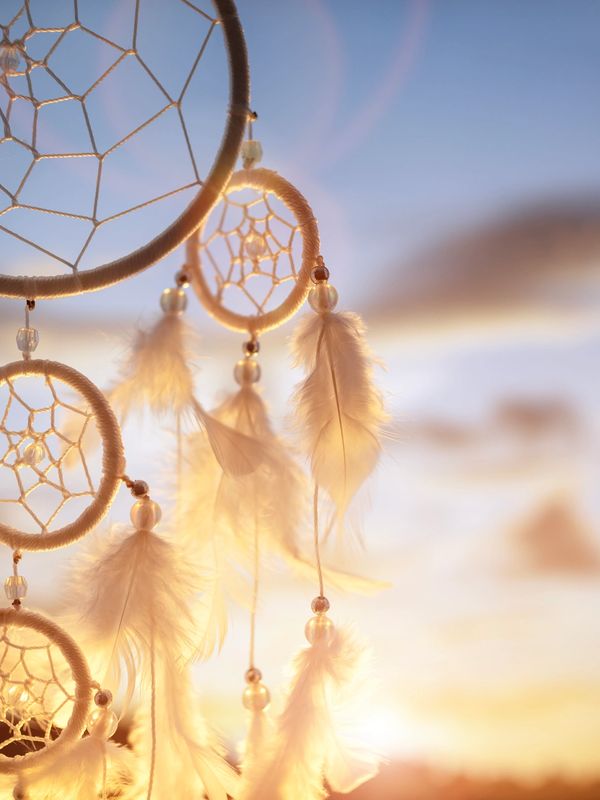Close-up of a dreamcatcher with feathers at sunset.