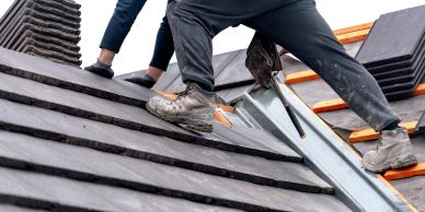 Workers installing roof tiles on a sloped roof.