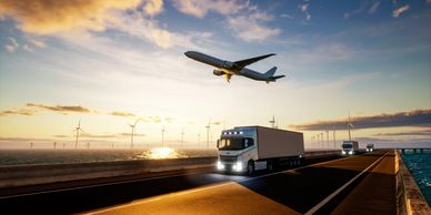 Truck driving on highway with airplane overhead at sunset.