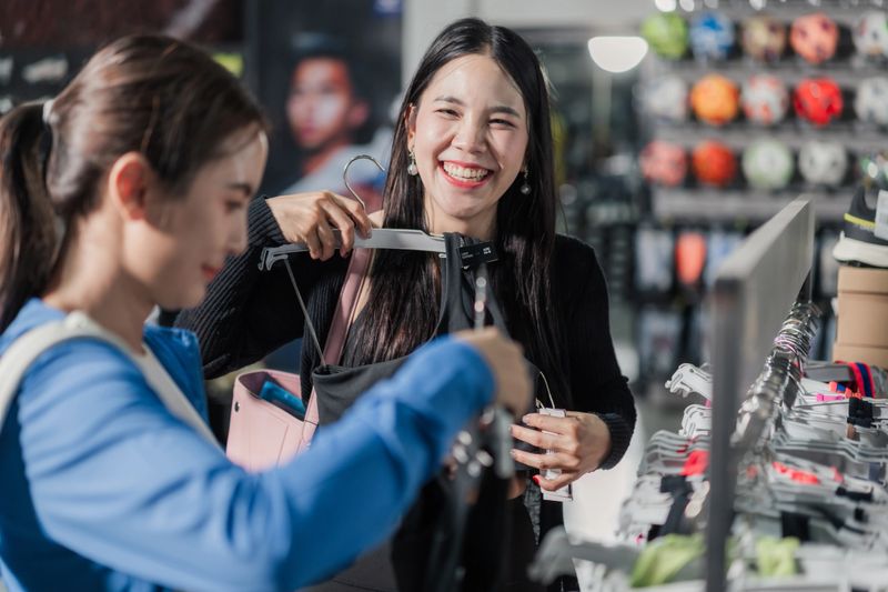 Asian woman smiling while holding sport bra in shop. Fitness fashion shopping, activewear, retail experience, sport clothing, consumer lifestyle, modern sport store.