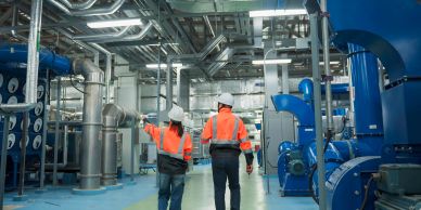 Two workers inspect equipment in an industrial facility.