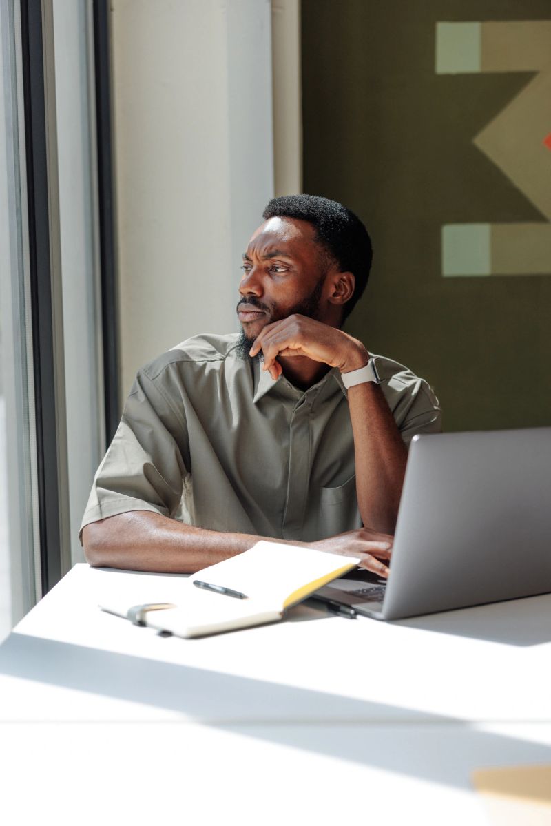 Young businessman sitting at his desk, looking thoughtfully out the window, contemplating a decision or considering new ideas