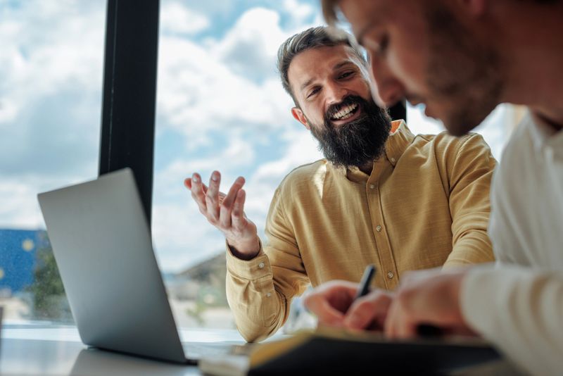 Business partners engaged in a lively discussion about a project while collaborating in front of a laptop in a modern office setting
