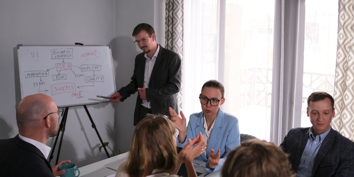 Business team discussing strategy with whiteboard presentation in office meeting.