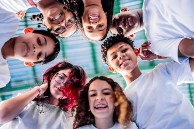 A group of smiling diverse teens looking down at the camera in white shirts.