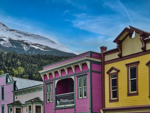 Colorful buildings with mountain and forest backdrop under a blue sky.